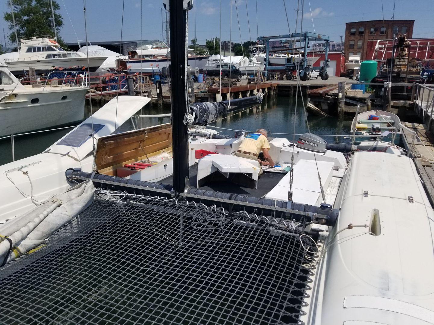 Captain Joe attaching engine controls at start of season.  Note engine cover is off and on trampoline.  See solar charger on cabin top open.